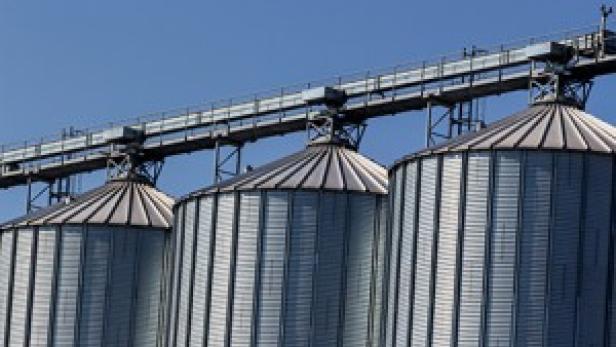 Drei Getreidesilos aus Metall unter einem blauen Himmel.