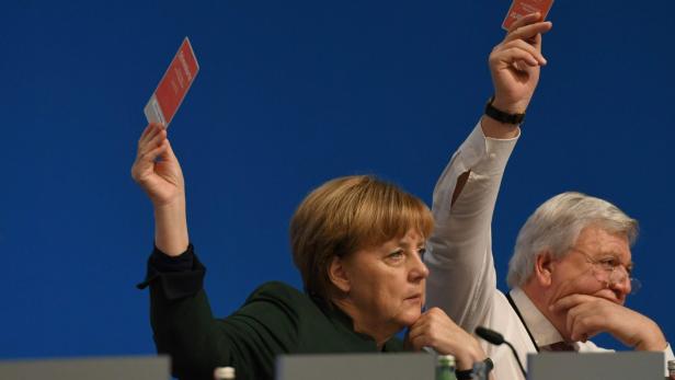 Angela Merkel und ein Mann heben während einer Abstimmung ihre Stimmkarten.