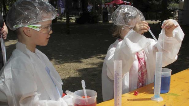 Zwei Kinder in Laborkitteln experimentieren mit Flüssigkeiten und Messbechern.