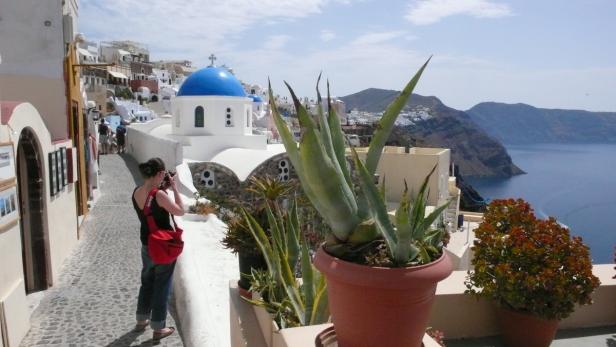 Eine Frau fotografiert die typisch griechische Architektur mit blauem Kirchendach in Santorin.