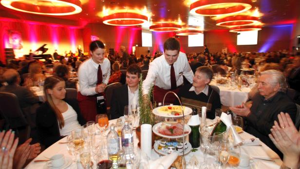 In einem festlichen Saal werden Gäste von Kellnern bedient.