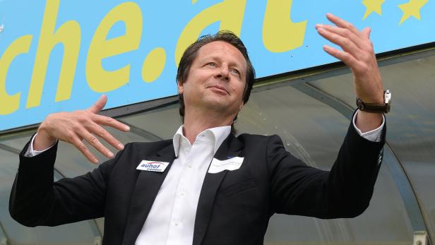 Ein Mann in Anzug gestikuliert vor einer Werbetafel.