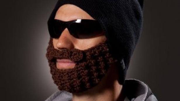 Ein Mann mit Sonnenbrille und einer schwarzen Mütze mit angehäkelten, braunen Bart.