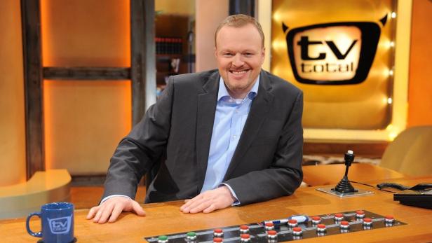 Ein lächelnder Mann sitzt am Schreibtisch im Studio von „TV total“.