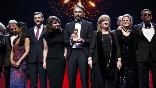 Eine Gruppe von Personen steht auf einer Bühne, ein Mann hält einen goldenen Bären in den Händen.