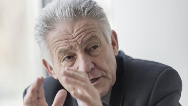 Ein älterer Mann mit grauen Haaren gestikuliert mit seinen Händen.