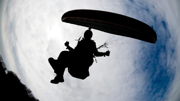 Die Silhouette eines Gleitschirmfliegers vor einem bewölkten Himmel.