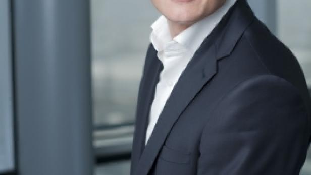 Ein Mann mit Brille und dunklem Anzug lächelt in die Kamera.