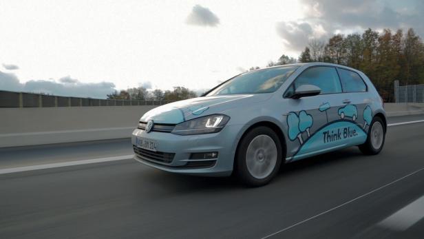 Ein silberner VW Golf mit „Think Blue“-Aufdruck fährt auf einer Autobahn.