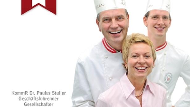 Eine Frau hält eine Sachertorte, flankiert von zwei Bäckermeistern des Heiner-Teams.