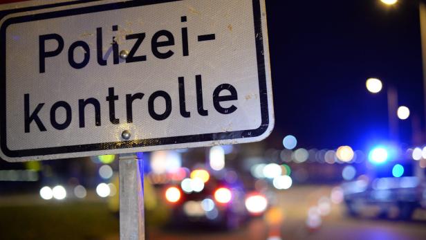 Ein Schild „Polizeikontrolle“ bei Nacht mit Blaulicht im Hintergrund.