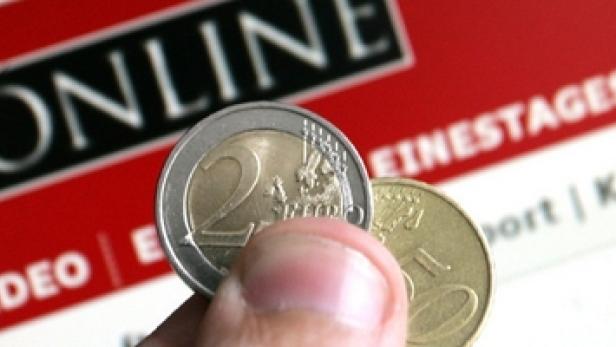 Eine Hand hält eine 2-Euro-Münze vor dem Hintergrund einer Online-Zeitung.