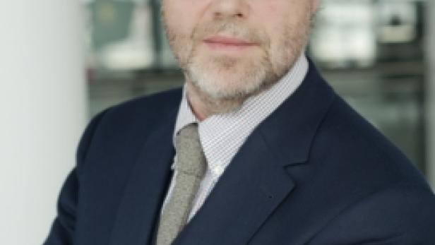 Ein Mann mit Brille und Anzug steht mit verschränkten Armen da.