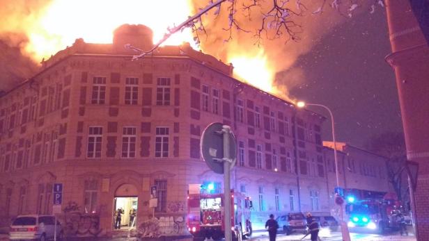 Ein großes Gebäude steht in Flammen, während Feuerwehrleute vor Ort sind.