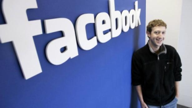 Mark Zuckerberg posiert vor dem Facebook-Logo.