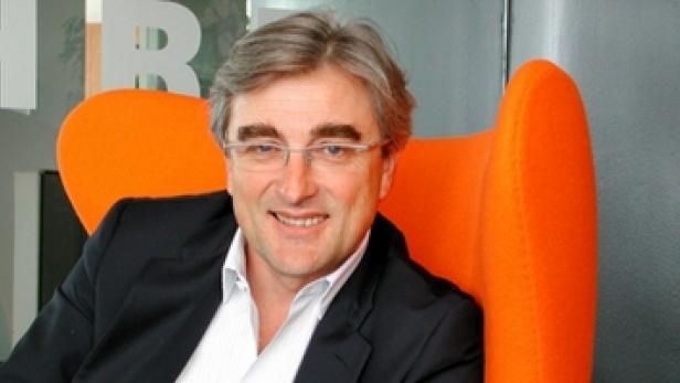 Ein Mann mit Brille sitzt in einem orangefarbenen Sessel.