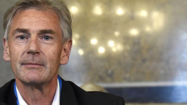 Porträt eines Mannes mit grauem Haar und einem dunklen Anzug.