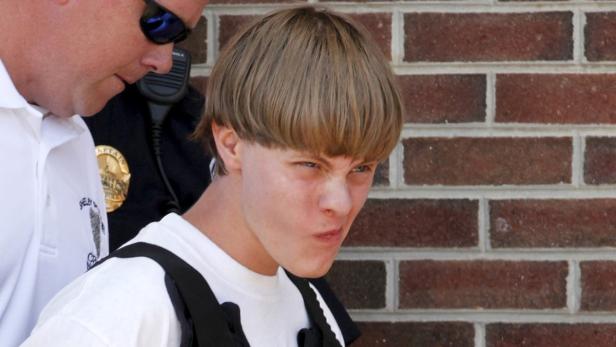 Ein junger Mann mit einem Bowl Cut wird von einem Polizisten begleitet.