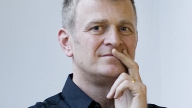 Ein Mann mittleren Alters mit grauem Haar berührt nachdenklich sein Kinn.