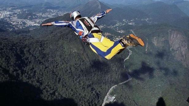 Ein Basejumper springt von einem Felsen in eine grüne Landschaft.