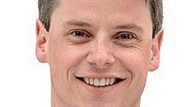Ein lächelnder Mann im Anzug vor einem weißen Hintergrund.
