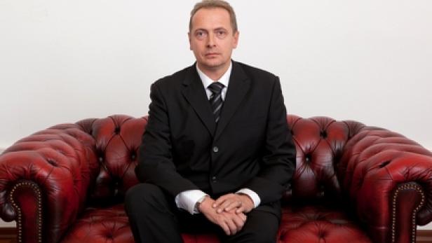 Ein Mann im Anzug sitzt auf einem roten Ledersofa.
