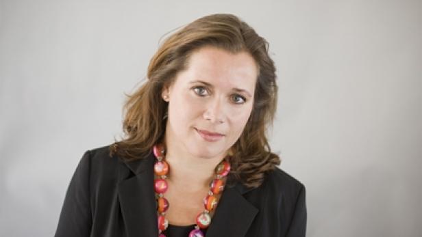 Eine Frau mit braunen Haaren und einer bunten Halskette vor einem grauen Hintergrund.