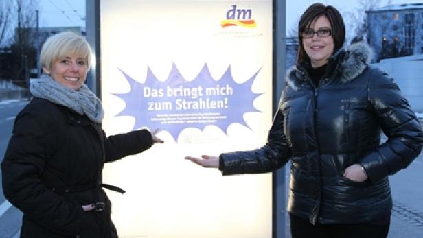 Zwei Frauen präsentieren eine DM-Werbung mit dem Slogan „Das bringt mich zum Strahlen!".