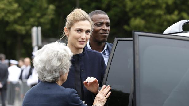 Eine Frau wird von einer älteren Dame an einem Auto begrüßt, im Hintergrund ein Mann.
