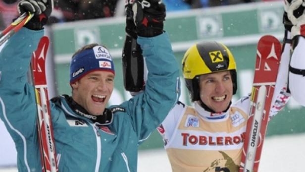 Zwei Skirennläufer jubeln mit erhobenen Armen und Skiern in der Hand.