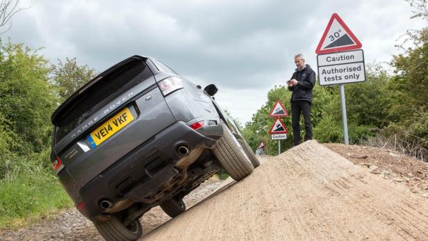 Ein grauer Range Rover fährt eine steile Rampe hoch, während ein Mann zusieht.