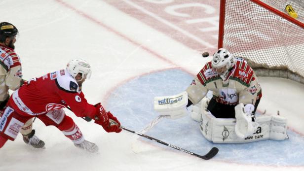 Ein Eishockeyspieler in Rot schießt auf das Tor, das von einem Torwart verteidigt wird.