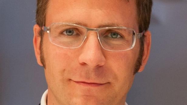 Ein Mann mit Brille, weißem Hemd und dunklem Sakko blickt in die Kamera.