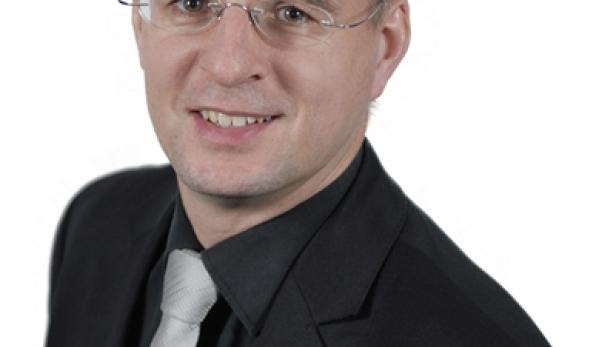 Ein Mann mit Brille und Anzug lächelt in die Kamera.