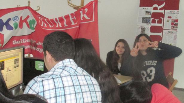 Jugendliche sitzen vor einem Computer mit einem „KiKo Kurier“-Banner im Hintergrund.