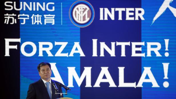 Ein Mann in Anzug steht vor einem Bildschirm mit dem Inter Mailand Logo und dem Slogan „Forza Inter! Amala!“.