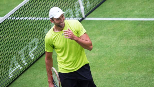 Ein Tennisspieler mit Tennisschläger lächelt auf einem Tennisplatz.
