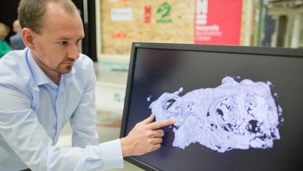 Ein Mann zeigt auf einem Bildschirm ein 3D-Modell eines Schädels.