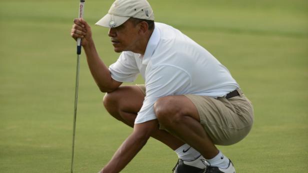 Barack Obama kauert auf einem Golfplatz und zielt mit einem Putter auf den Ball.