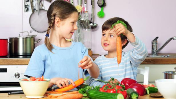Zwei Kinder bereiten in der Küche Gemüse zu.