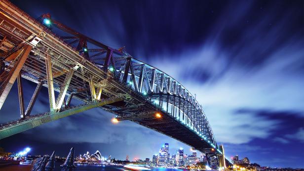 Die beleuchtete Sydney Harbour Bridge überspannt das Wasser bei Nacht.