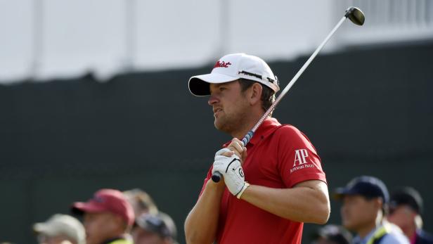 Ein Golfspieler in rotem Hemd und weißer Kappe hält einen Golfschläger.