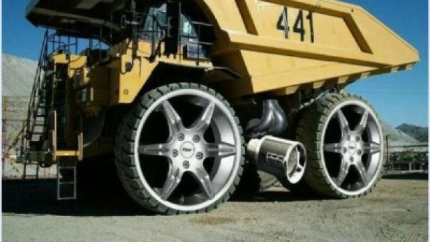 Ein gelber Muldenkipper mit großen, auffälligen Felgen steht auf einer Baustelle.