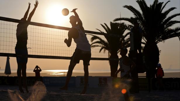 Bei Sonnenuntergang spielen zwei Teams Beachvolleyball am Strand.
