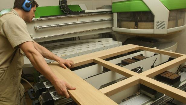 Ein Mann mit Kopfhörern arbeitet an einer Holzbearbeitungsmaschine.