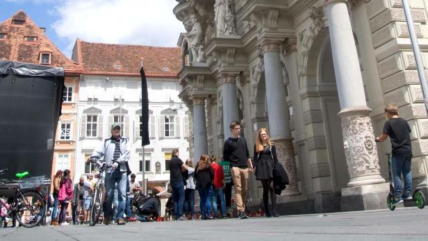 Menschen versammeln sich vor einem Gebäude mit Säulen in Graz.