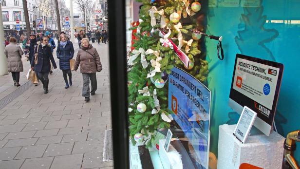 Passanten gehen an einem Schaufenster mit Weihnachtsdekoration und Elektronikartikeln vorbei.