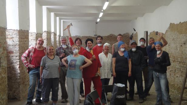 Eine Gruppe von Menschen steht in einem Raum mit freigelegten Ziegelwänden und hält Hämmer.