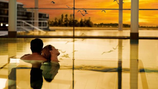 Ein Paar entspannt in einem Pool mit Blick auf einen Sonnenuntergang.