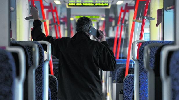 Ein Mann telefoniert in einem öffentlichen Verkehrsmittel und hält sich fest.